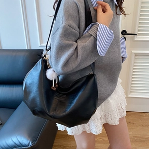 Chic black oversized hobo bag in textured leather with a cute white plush pompom charm