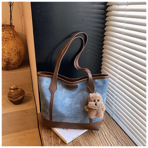 Dettaglio della borsa tote in denim blu con finiture in pelle marrone e ciondolo orso