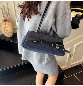 Detail of dark blue denim shoulder bag featuring black leather straps and silver buckles