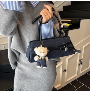 Detail of blue denim shoulder bag with leather straps and cute plush bear charm