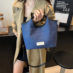 Fashionable denim tote bag with black leather handles and long adjustable shoulder strap