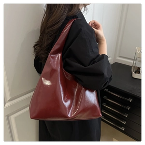 Back view of a model wearing a burgundy high-gloss patent leather hobo shoulder bag