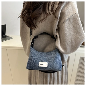 Detailed shot of retro denim crossbody bag featuring black leather handles and label