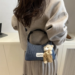Chic blue denim crescent crossbody bag for women with a cute plush bear charm accessory