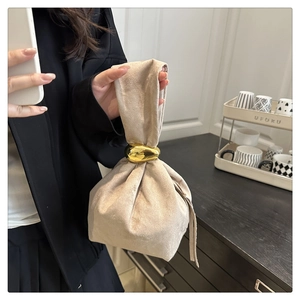 Detail of a beige suede handbag featuring a modern gold metallic ring handle design