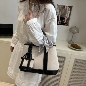 Fashionable beige canvas tote bag with black leather trim and decorative silk scarf detail