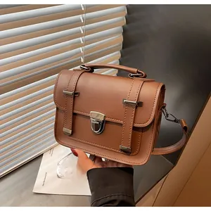 Détail du sac messager en cuir marron avec poignée supérieure et boucle de fermeture métal