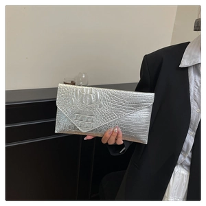 Close-up of a silver envelope clutch bag with crocodile texture held by a model