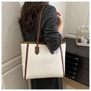Detailed view of large woven tote bag with brown leather trim carried by a model