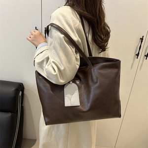 Large dark brown tote bag with vintage leather texture and decorative tag on model shoulder