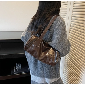 Detail view of a dark brown glossy leather baguette bag worn over the shoulder by a model