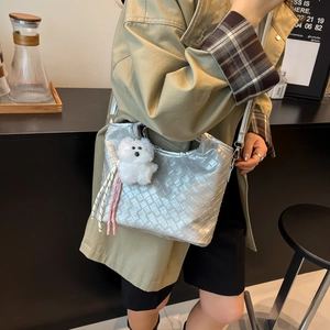 Chic silver woven shoulder bag with plush dog charm and tassels on an olive coat model