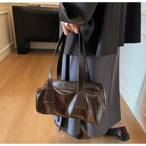 Detail of deep brown retro cylindrical tote bag featuring glossy wax leather texture