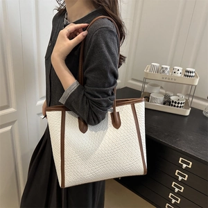White woven tote bag with brown leather trim shown on a shoulder in a home setting