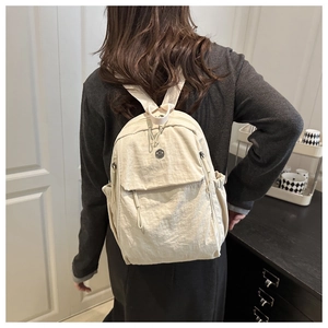 Détail du sac à dos en nylon crème avec fermetures éclair incurvées et poches latérales