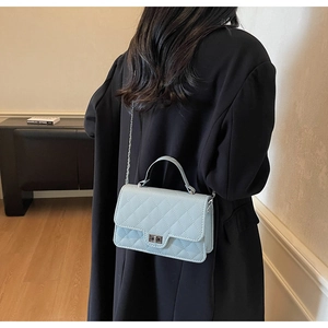 Detail of light blue quilted chain bag with silver twist lock on black coat model