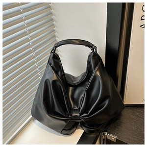 Detailed view of black faux leather tote featuring a large bow and soft pleated texture