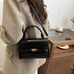 Minimalist black leather crossbody bag with gold buckle in an elegant indoor cafe setting