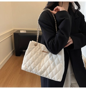 Detail of white quilted tote bag with golden chain strap on model in black suit