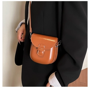 Macro detail of glossy caramel patent leather saddle bag with silver hardware and clean stitching