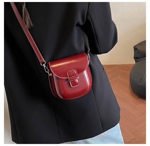Detail view of burgundy glossy leather crossbody bag worn over a black blazer jacket