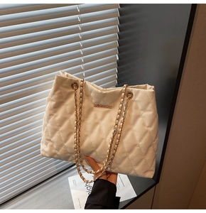 Detailed view of beige quilted tote bag with gold chain strap and luxury metal logo