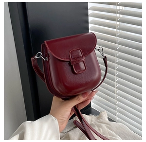 Detailed macro view of the burgundy faux leather texture and silver hardware of the crossbody bag