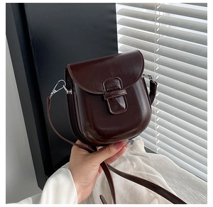Macro detail of the dark brown leather saddle bag flap with brand logo engraving