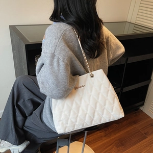 White quilted tote bag with gold chain strap and metal logo worn by a model in interior