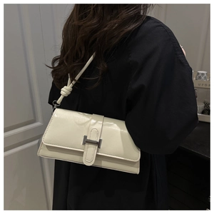 Detail of a creamy white rectangular shoulder bag with square metal buckle and knotted strap