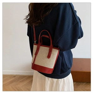 Detailed back view of a beige canvas bucket bag with burgundy leather trim on a model