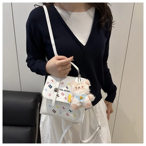 Détail du sac bandoulière blanc avec motifs graffiti colorés et un charme d'ours en peluche