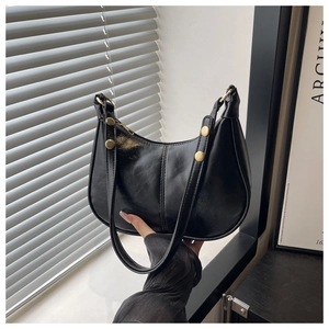 Close-up of black crescent shoulder bag with golden rivets and polished faux leather finish