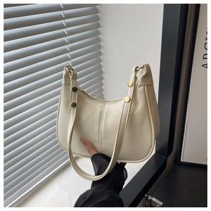 Close-up of beige half-moon hobo bag with gold metal rivets and smooth finish