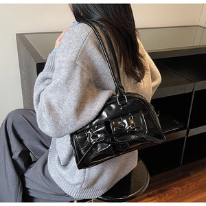 Model wearing a black glossy patent leather shoulder bag with a stylish bow decoration
