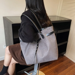 Chic grey suede tote bag with black leather straps shown on model from a side back view