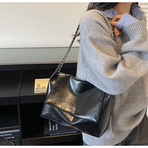 Chic black wrinkled leather shoulder bag with metal chain strap worn by a model