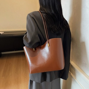 Elegante bolso tote de cuero marrón con detalles dorados llevado por modelo en chaqueta