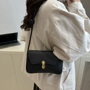 Minimalist black faux leather shoulder bag with gold metal clasp worn by a female model