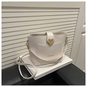 Close-up of cream white bucket bag featuring a gold heart clasp and litchi grain texture