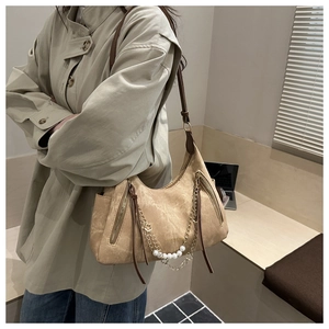 Detail of beige suede tote bag with brown leather strap and elegant pearl chain ornament