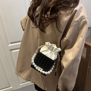 Mini sac seau avec corps tissé, poignée en perles et bandoulière dorée porté par un mannequin