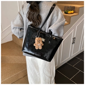 Detalle de bolso tote negro brillante con correas finas y un colgante de oso de peluche café