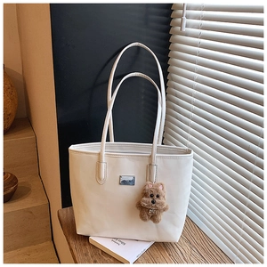 Detalle del bolso tote de cuero brillante blanco crema con un tierno amuleto de osito