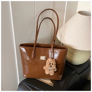 Detalle de bolso tote marrón brillante con un lindo colgante de peluche y placa plateada
