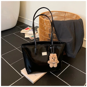 Detalle de bolso tote de charol negro con placa plateada y adorno de oso marrón