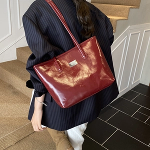 Bolso tote minimalista de charol burdeos brillante con logo metálico para uso cotidiano