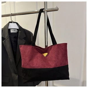 Detalle del bolso tote de ante burdeos y negro con el distintivo emblema dorado frontal