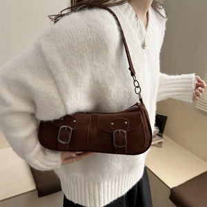 Brown suede underarm bag with metal buckles shown on a model in white sweater