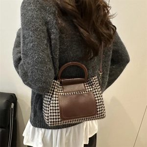 Classic houndstooth patterned Boston bag with brown leather handles worn by a model